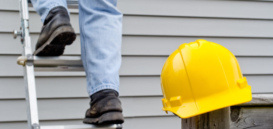 Yellow,hardhat,on,railing,post,with,worker's,legs,on,ladder